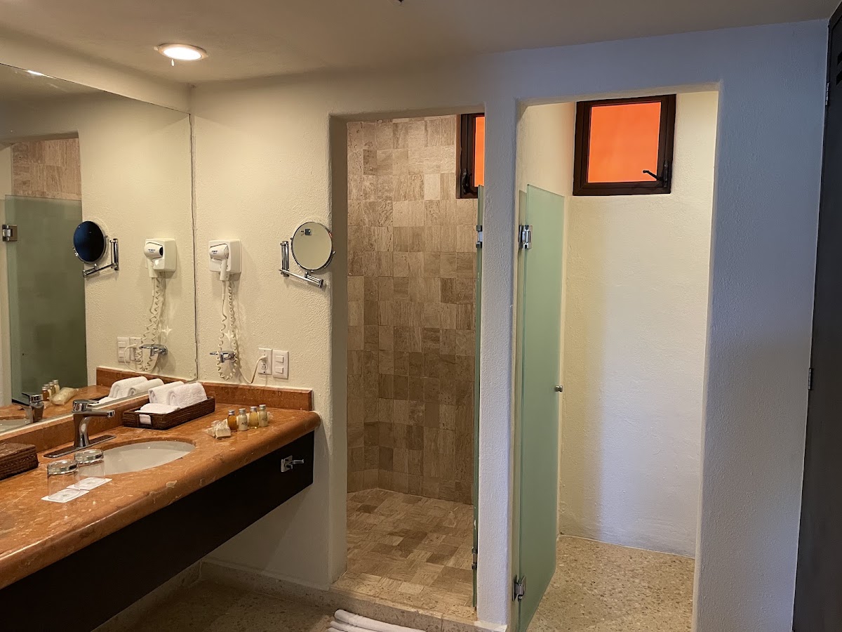 Resort bathroom with wooden vanity, large mirror, walk-in shower with tile walls, and amenities arranged on countertop.