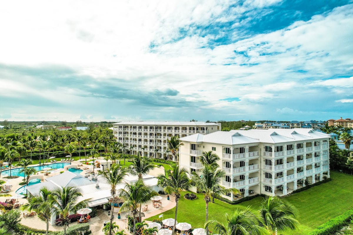 Alexandra Resort multi-story pastel buildings overlook pools, palm trees, and manicured lawns under a partly cloudy sky.