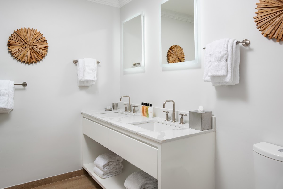 Modern bathroom with dual vanity, white countertop, brushed nickel fixtures, and woven circular wall decor at Alexandra Resort.