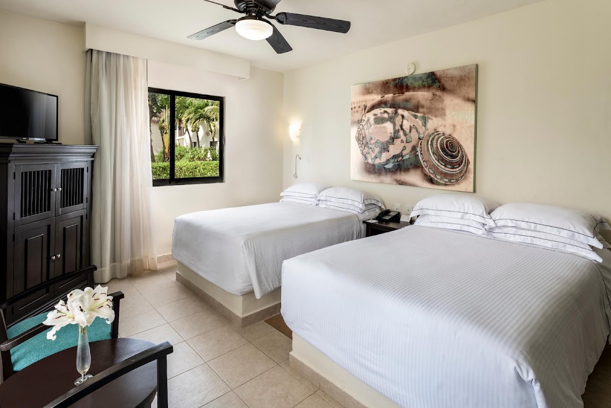 Guest room with two queen beds, black ceiling fan, dark wood cabinet, and window overlooking tropical grounds at Allegro Cozumel.