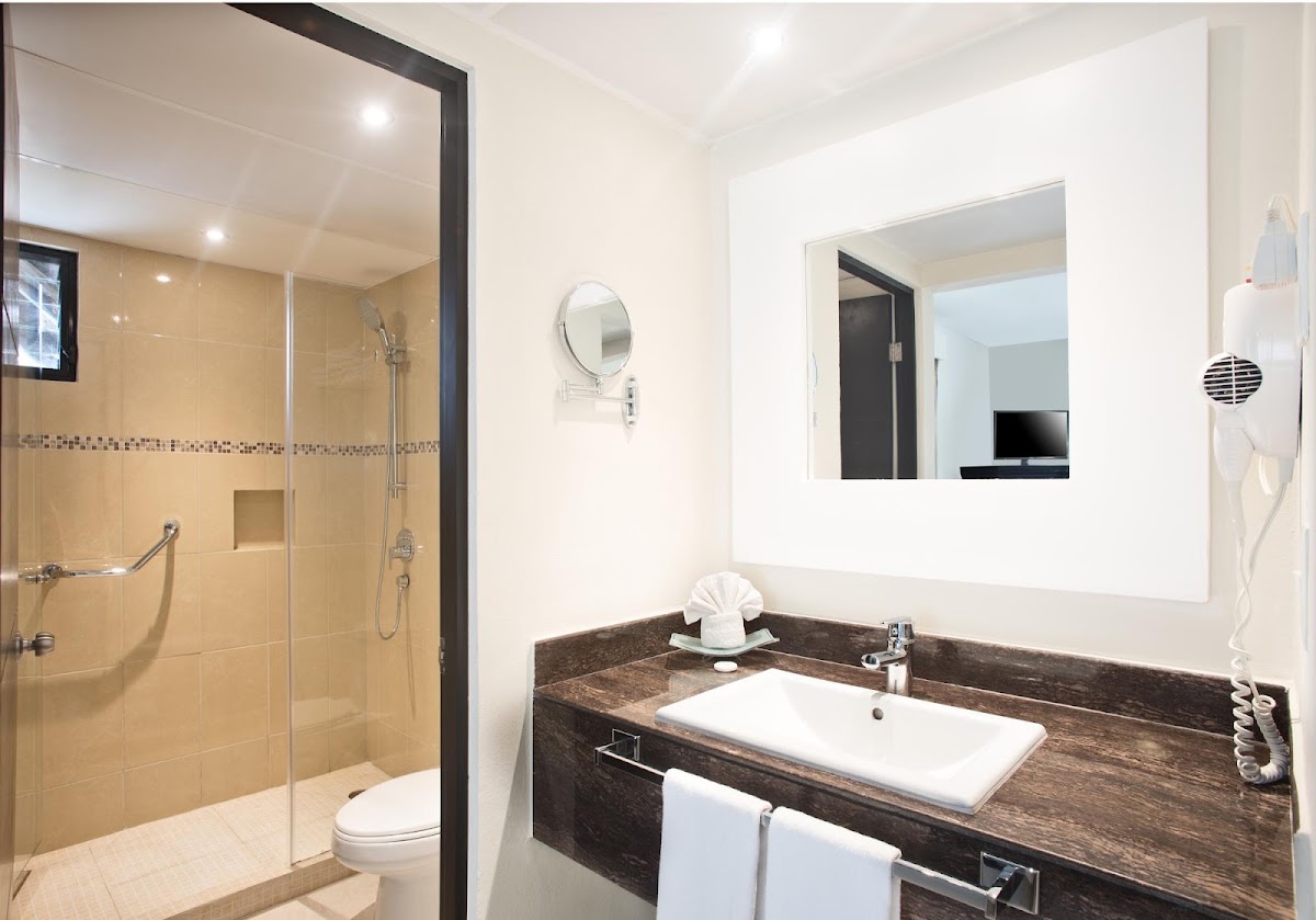 Modern bathroom with walk-in shower, dark wood vanity with white rectangular sink, and large illuminated mirror.