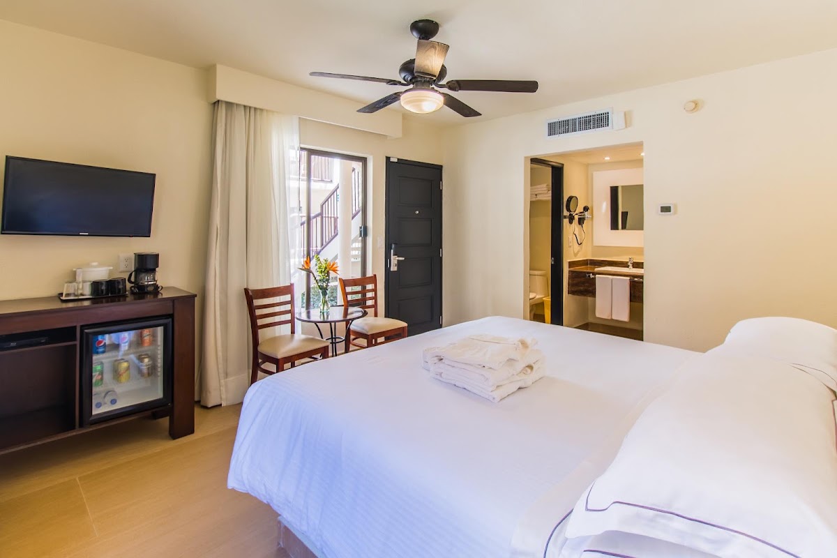 Resort guest room with two beds, flat-screen TV, mini-fridge, small dining table, and balcony door with ocean view.