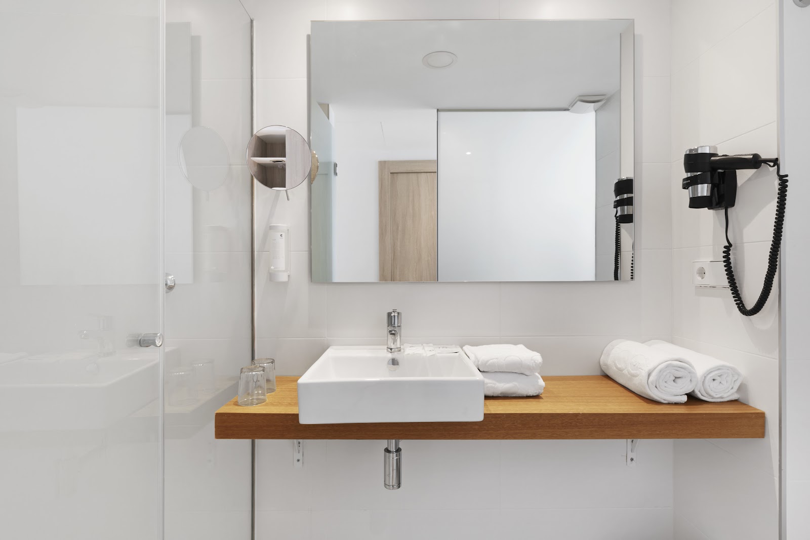 Modern bathroom with white rectangular sink on wooden vanity, folded white towels, large mirror, and shower enclosure with glass door.