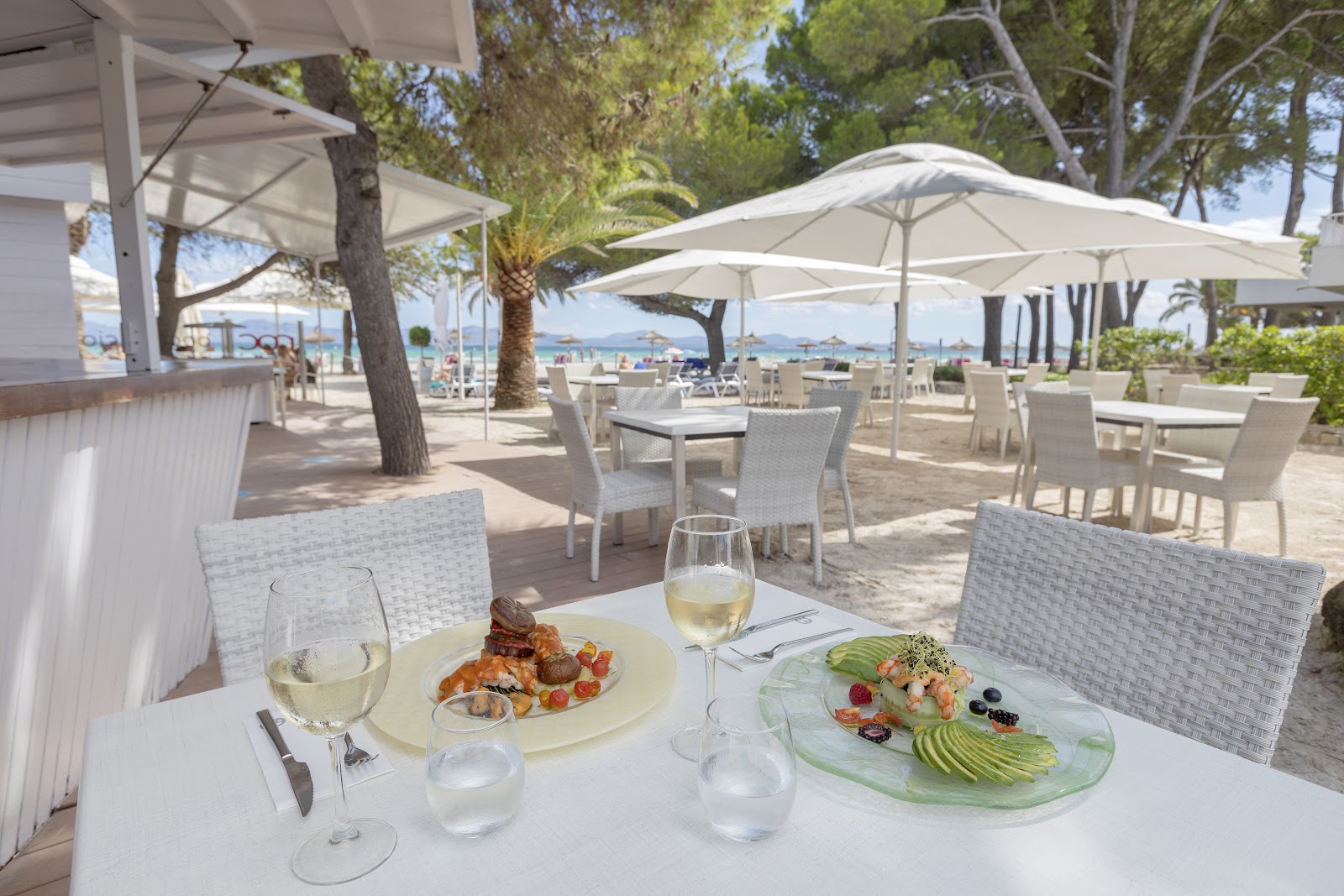 Beachfront dining table with plated appetizers and white wine overlooking the Mediterranean at Alua Boccaccio.