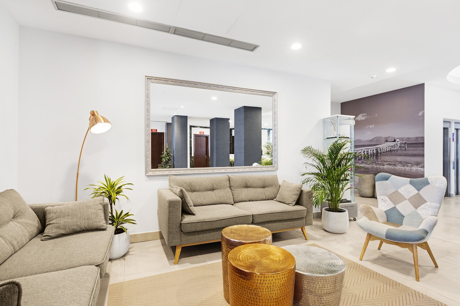 Modern lobby lounge with beige sofas, potted plants, gold accent tables, and a large mirror at Alua Boccaccio resort.