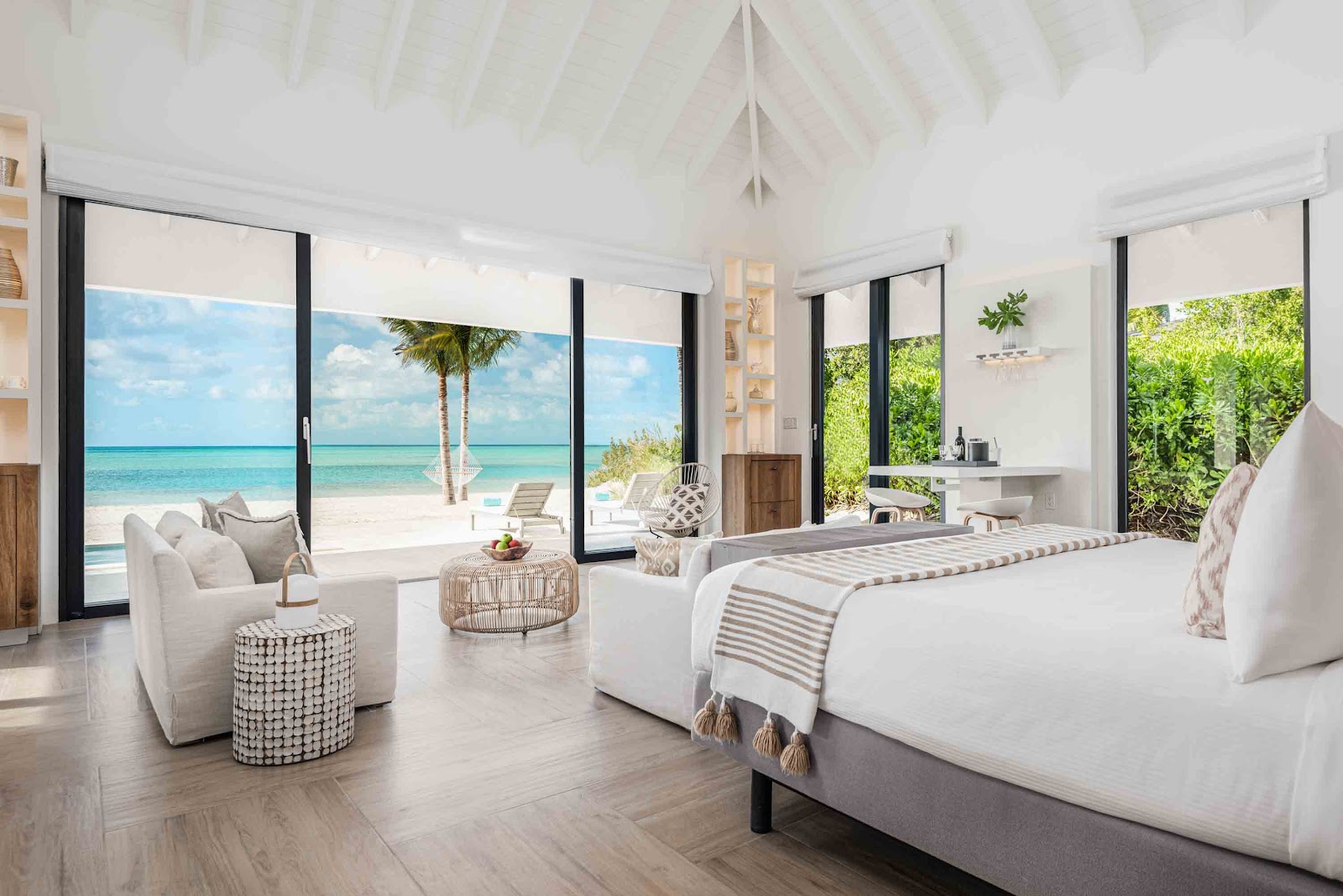 Beachfront villa bedroom at Ambergris Cay with king beds, white seating area, and turquoise ocean views through floor-to-ceiling windows.
