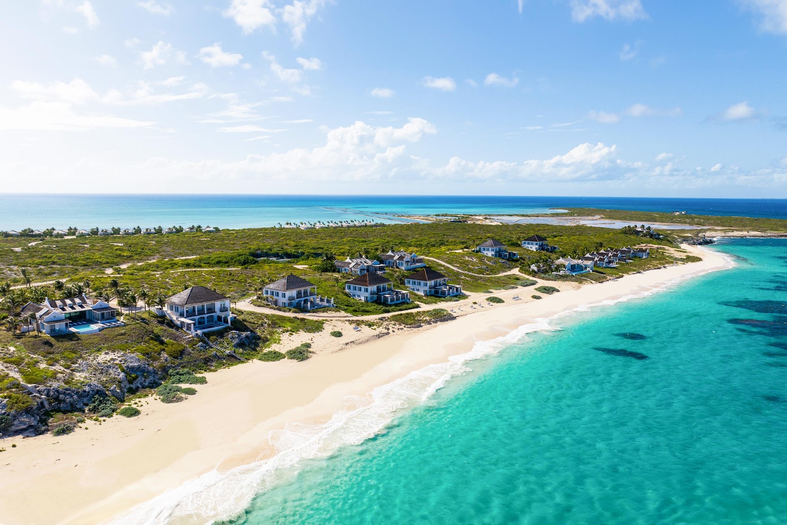 Aerial view of Ambergris Cay's beachfront villas nestled among vegetation, with turquoise waters and white sand beach below.