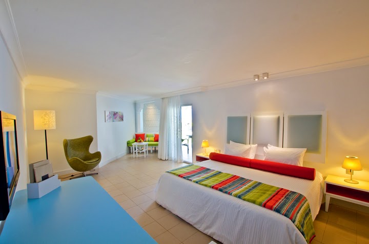 Modern resort room with two beds, colorful striped throw, seating area, and balcony at Ambre, A Sunlife Resort.