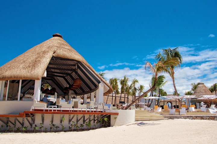 Beachfront cabana with thatched roof and striped awning at Ambre, A Sunlife Resort, with palm trees and lounge chairs visible along the sand.