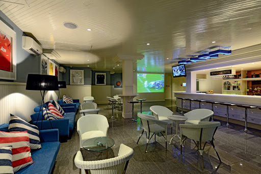 Ambre, A Sunlife Resort lounge with blue armchairs, dining tables, TV screens, and nautical decor on cream and green walls.
