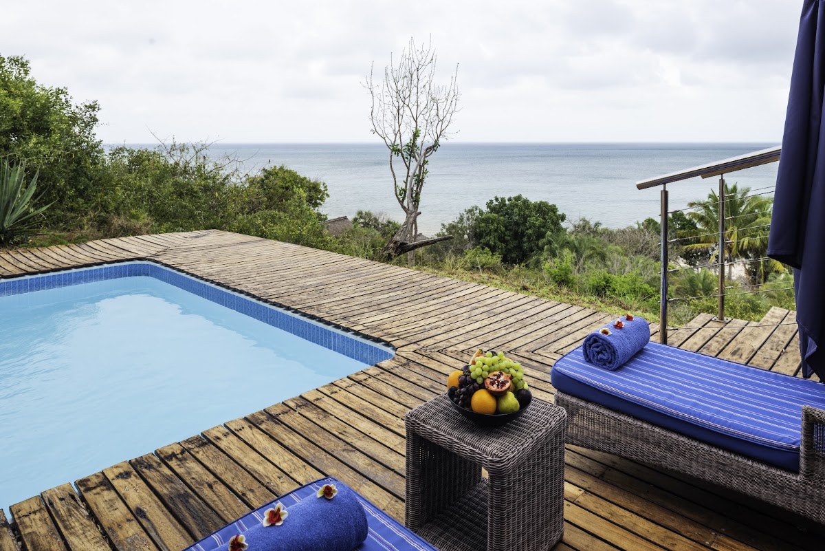 Wooden deck with blue pool, loungers, and ocean view at Anantara Bazaruto Island Resort overlooking tropical vegetation and calm sea.