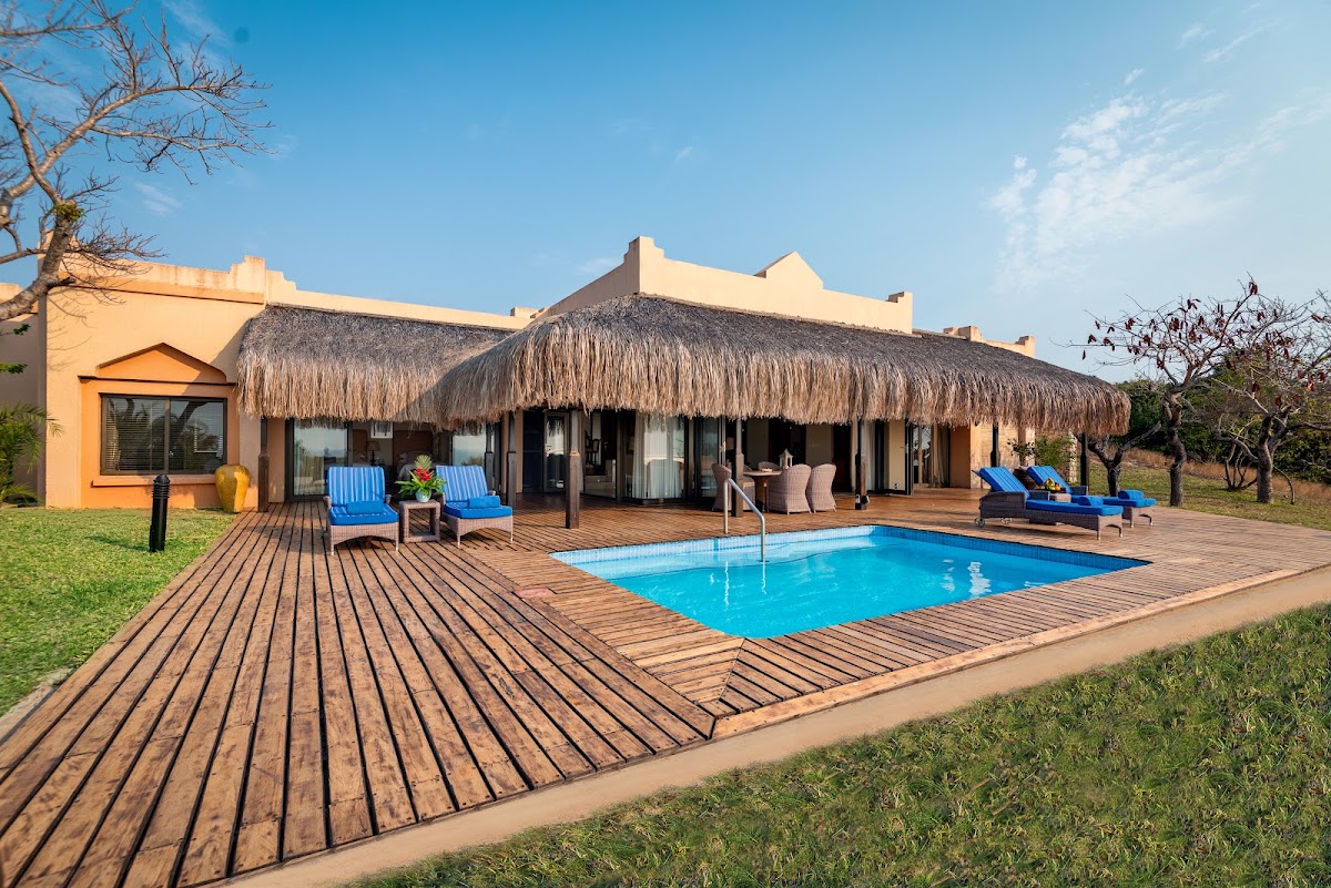 Thatched-roof bungalow with blue lounge chairs on wooden deck beside rectangular pool at Anantara Bazaruto Island Resort.