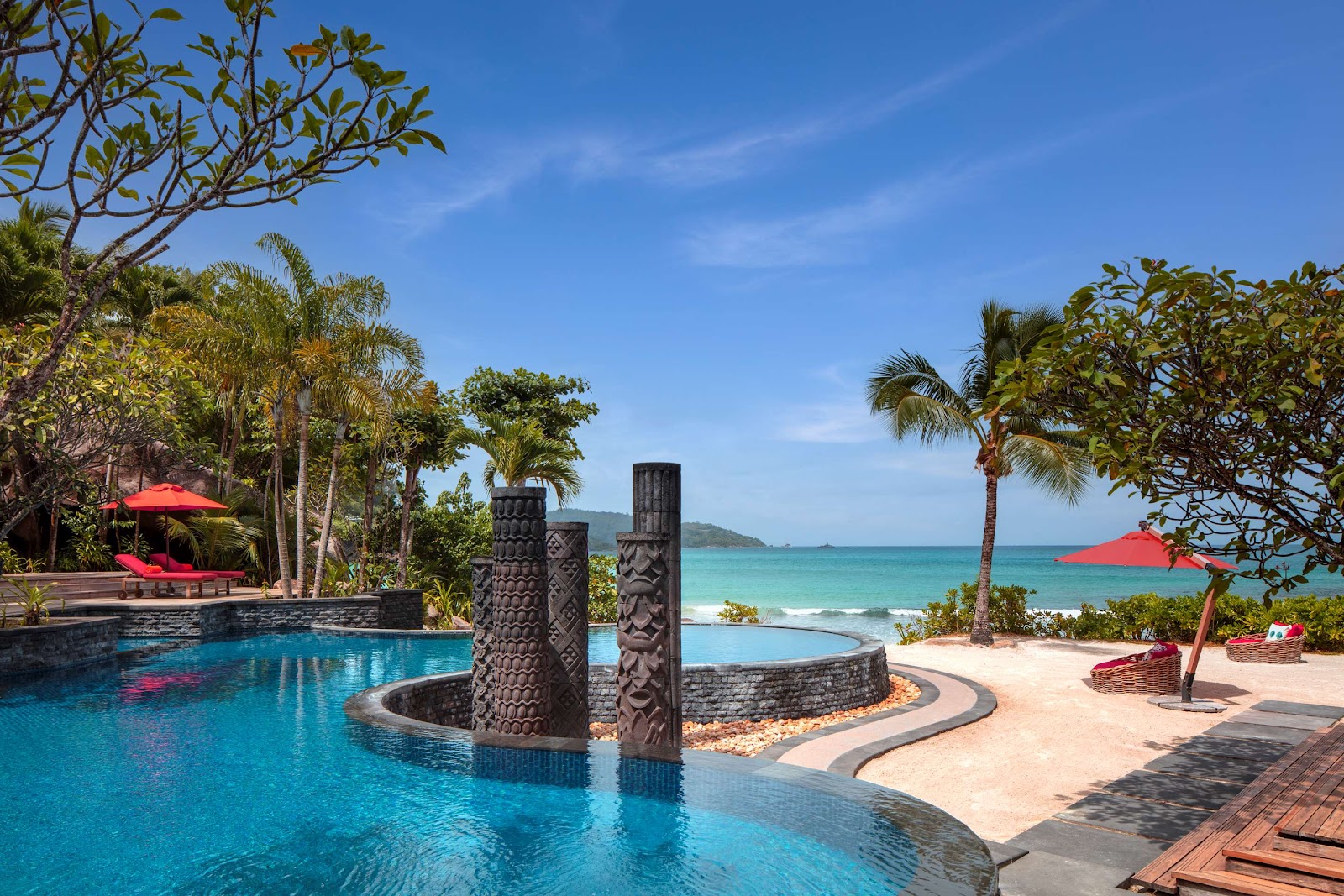 Infinity pool overlooking turquoise bay and white sand beach at Anantara Maia Seychelles Villas, with villa terrace and tropical forest beyond.
