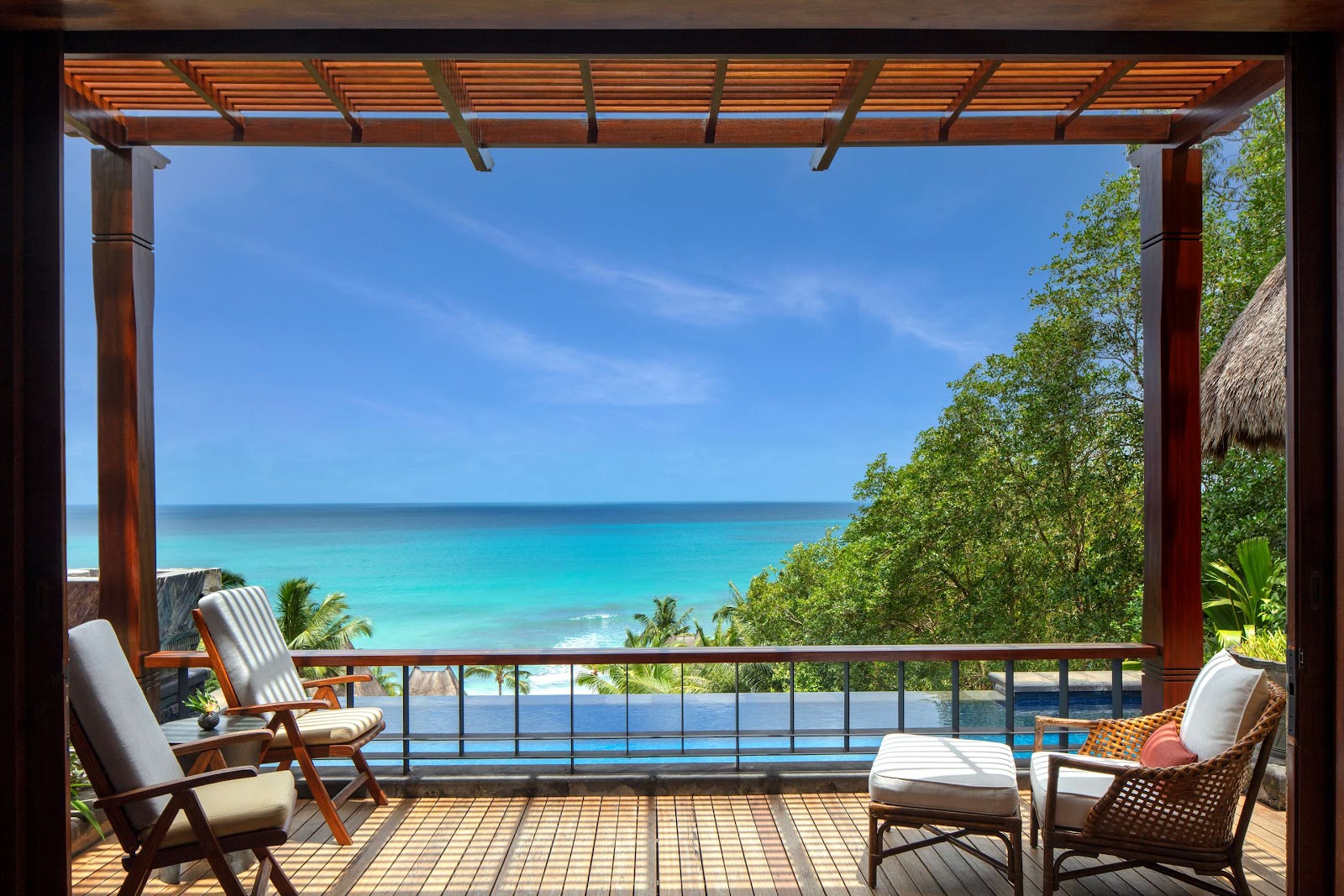 Thatched-roof bungalows with conical peaks overlook a turquoise pool at Anantara Maia Seychelles Villas, surrounded by tropical vegetation.