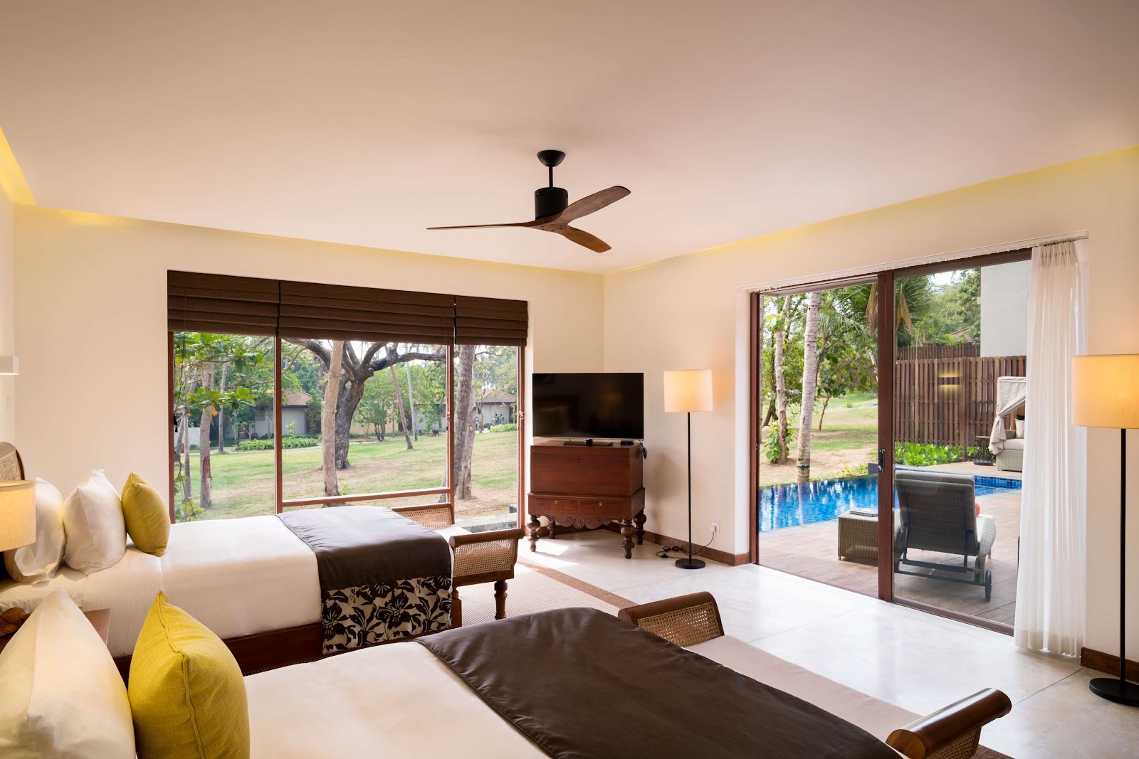 Resort suite at Anantara Peace Haven Tangalle with two beds, TV, and sliding doors opening to pool and palm-lined grounds.