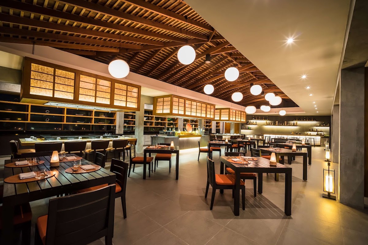 Modern resort restaurant with dark wood tables, orange chairs, slatted wooden ceiling, and pendant lights creating warm ambiance.