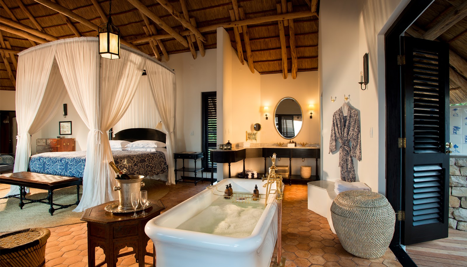 Spacious suite with canopied bed, soaking tub, vanity area, and wooden beam ceiling at andBeyond Benguerra Island.