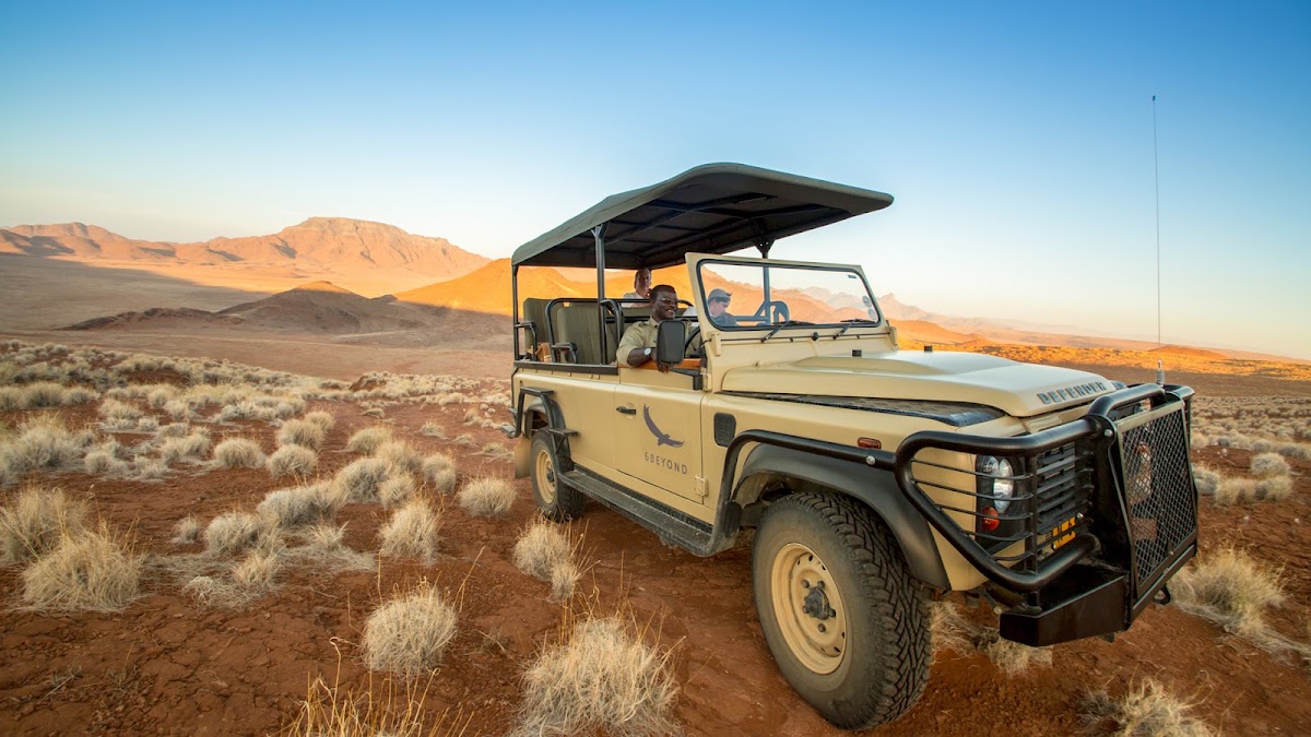 Safari vehicle with open-air canopy parked in desert scrubland with distant mountains under clear sky.