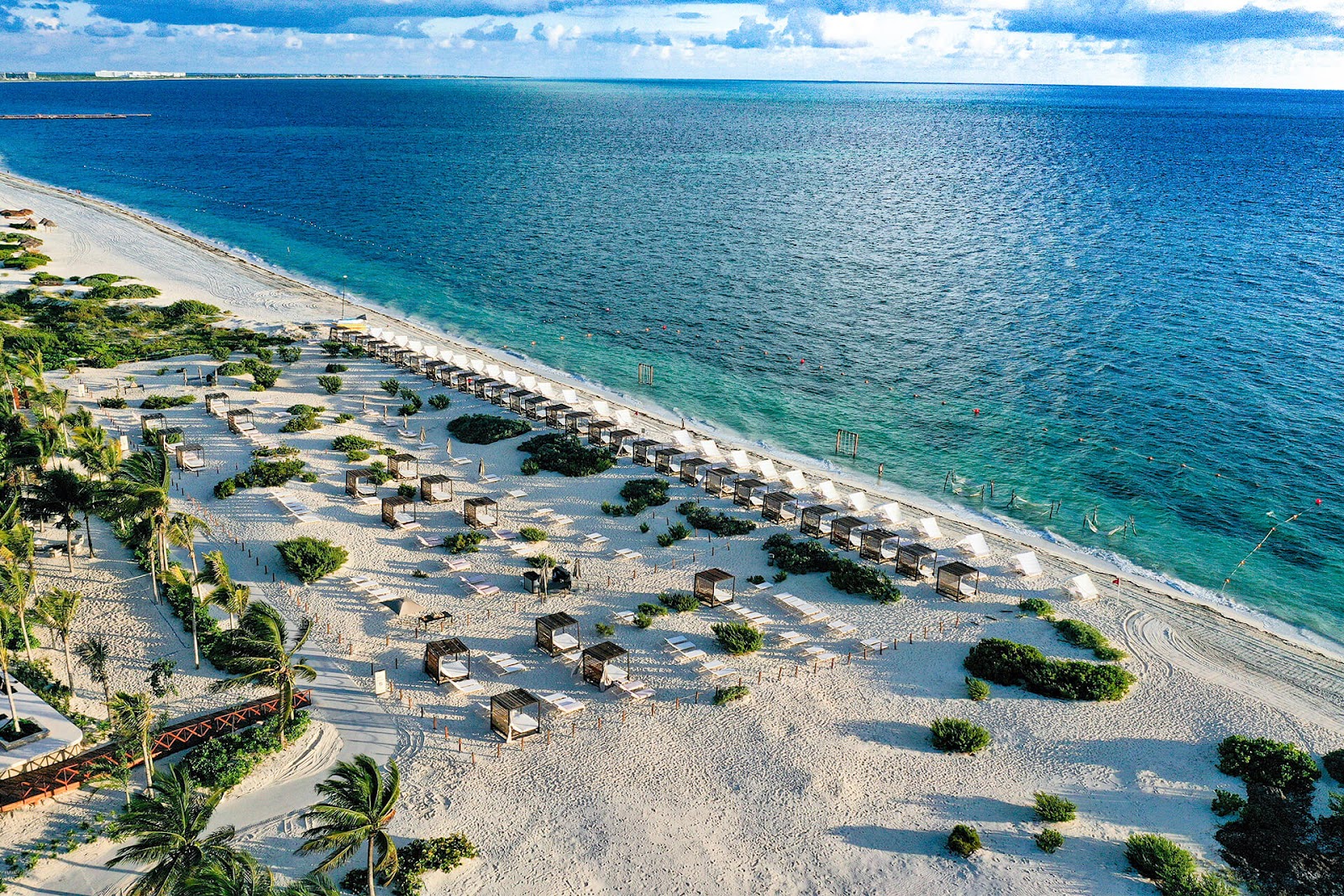 White sand beach with thatched cabanas and palm trees overlooking turquoise Caribbean waters at ATELIER Playa Mujeres.