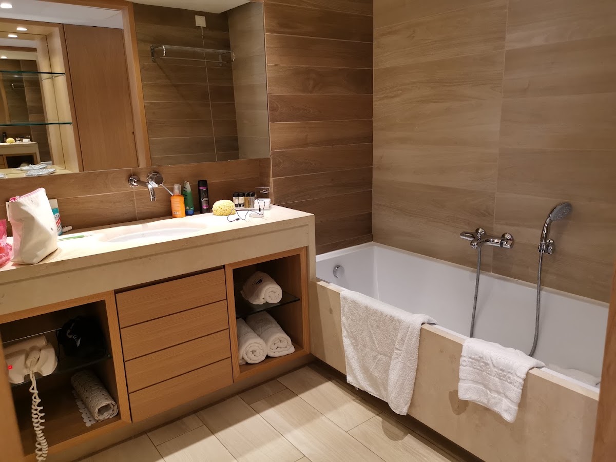 Bathroom with wood-tiled walls, white soaking tub, and wooden vanity stocked with toiletries and folded towels.