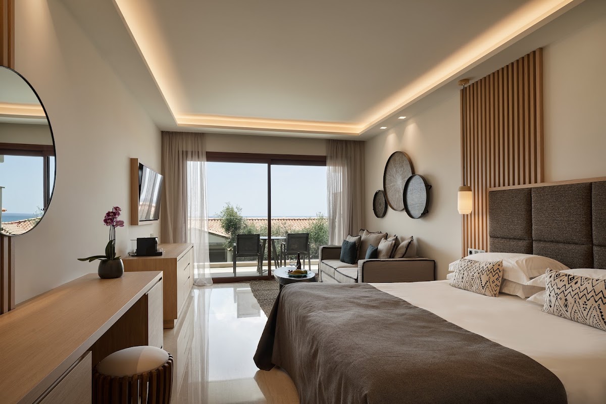 Modern resort bedroom with king bed, seating area, and ocean view through sliding glass doors to a balcony at Atlantica Imperial Resort and Spa.