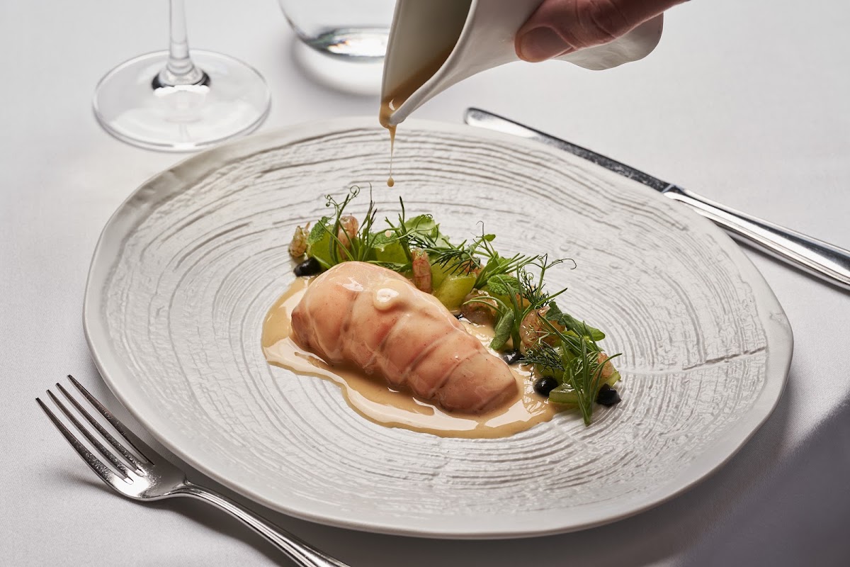 Chef drizzles sauce over sliced seafood and microgreens on a textured white plate at Atlantica Imperial Resort and Spa.