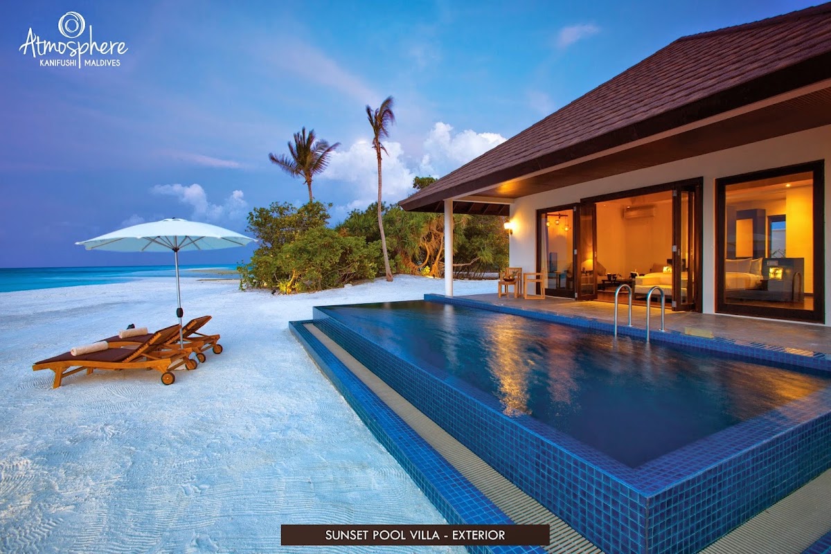 Sunset Pool Villa at Atmosphere Kanifushi features a blue tiled infinity pool, wooden lounge chairs, and white umbrella facing turquoise lagoon and palm trees.