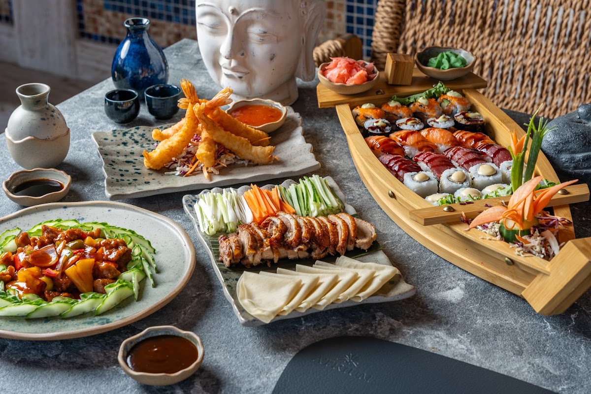 Dining spread at Atrium Palace with sushi rolls, tempura shrimp, sliced meats, fresh vegetables, and Asian decor on gray stone table.