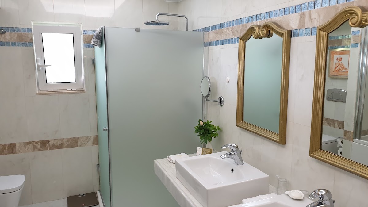 Bathroom at Atrium Prestige with white sink, gold-framed mirrors, glass shower enclosure, and blue tile accents.