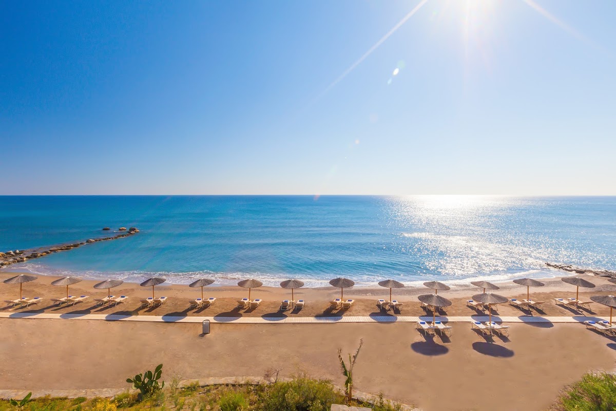 Rows of dark umbrellas and loungers line a sandy beach with clear turquoise water under bright blue sky at Atrium Prestige Thalasso Spa Resort.