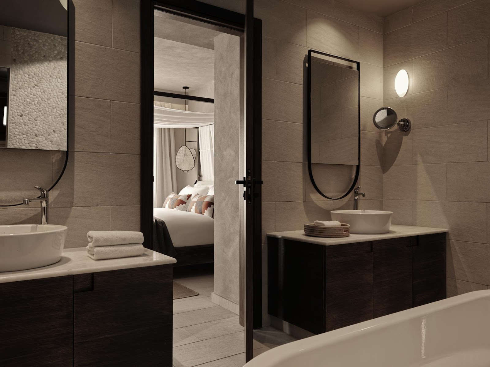 Modern bathroom with round vessel sinks, black-framed glass doors, and neutral tile walls opening to bedroom with white bedding.
