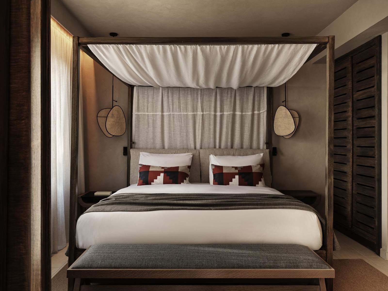 Four-poster bed with cream canopy drapes and woven hanging chairs in a neutral bedroom at Aulūs Lindos Rhodes Resort.