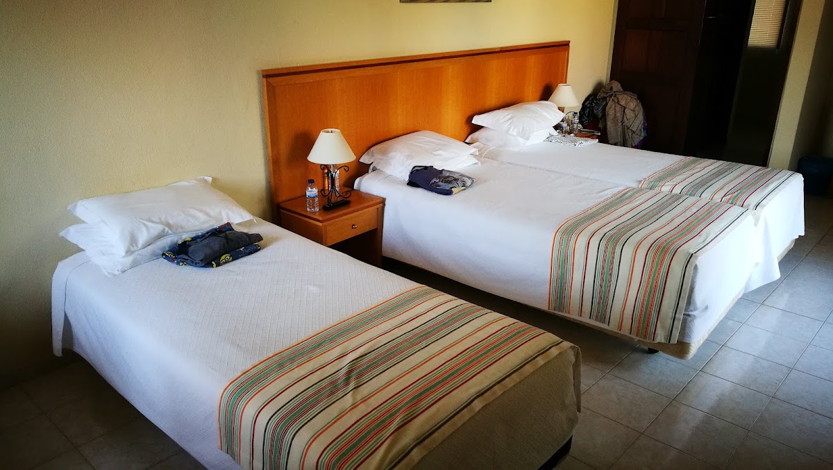 Resort hotel room with two double beds, orange wood headboard, white bedding, striped throws, and a nightstand with lamp between the beds.