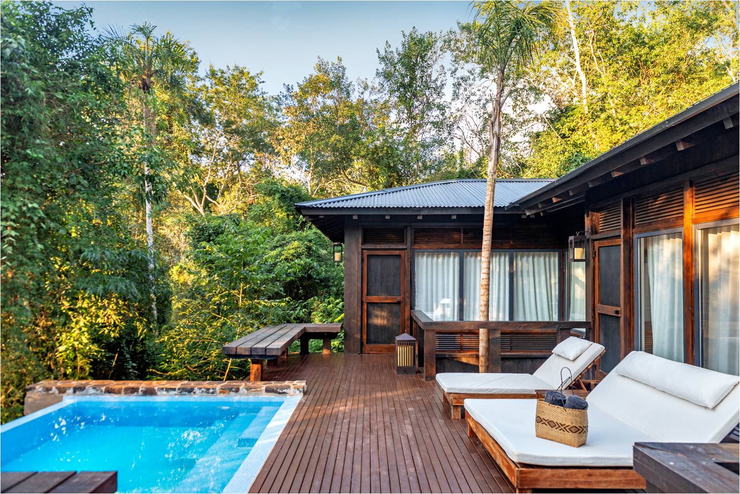 Dark wood villa with private pool and lounge chairs on a deck surrounded by lush forest canopy at Awasi Iguazú.