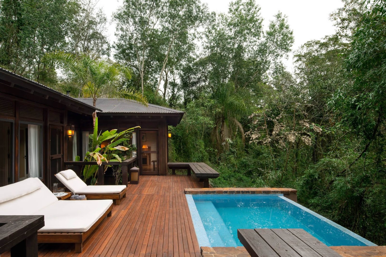 Private villa with wooden deck, lounge chairs, private pool, and dark wooden bungalow surrounded by dense forest at Awasi Iguazú.