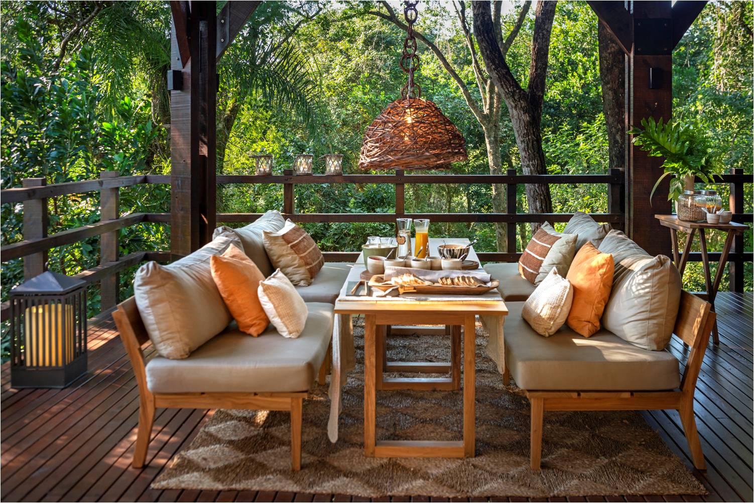 Wooden deck lounge area at Awasi Iguazú surrounded by dense green forest canopy, with upholstered seating, a woven pendant light, and refreshments on a low table.