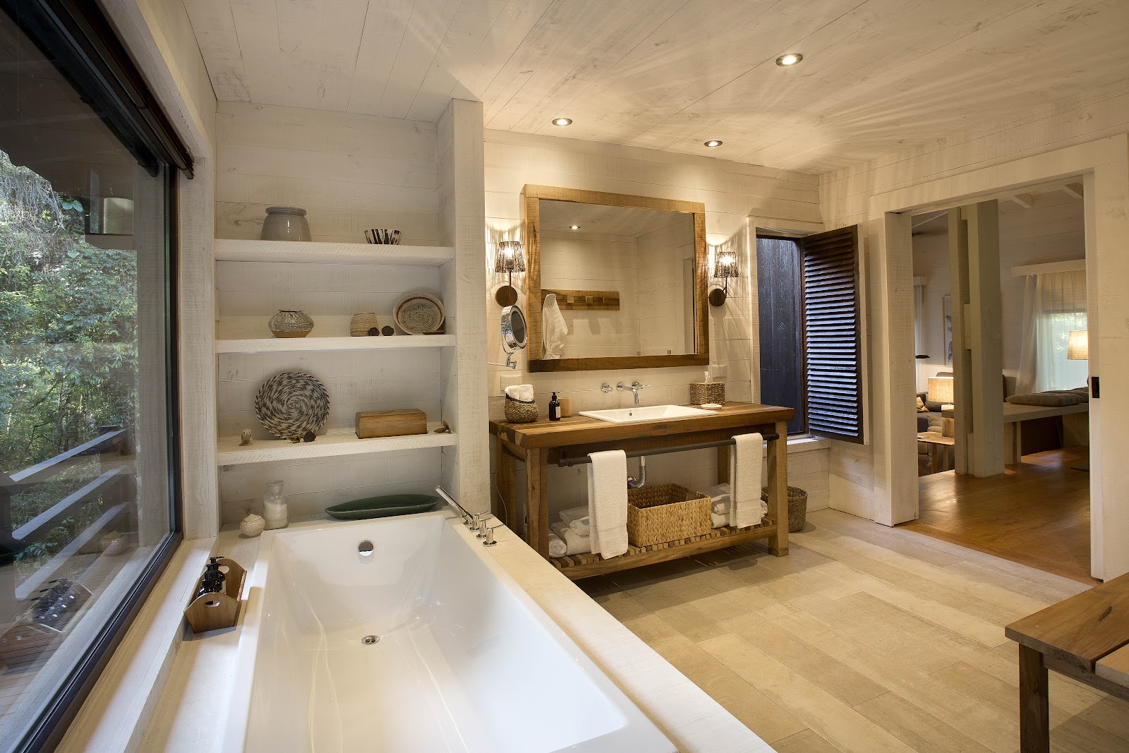 Spacious bathroom at Awasi Iguazú featuring a soaking tub, wooden vanity with mirror, built-in shelving, and access to the bedroom beyond.