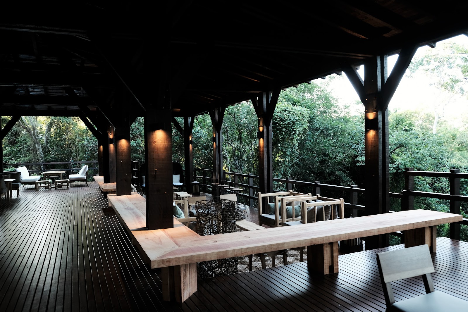 Covered wooden deck at Awasi Iguazú with dining table, lounge chairs, and forest views beyond the railing.