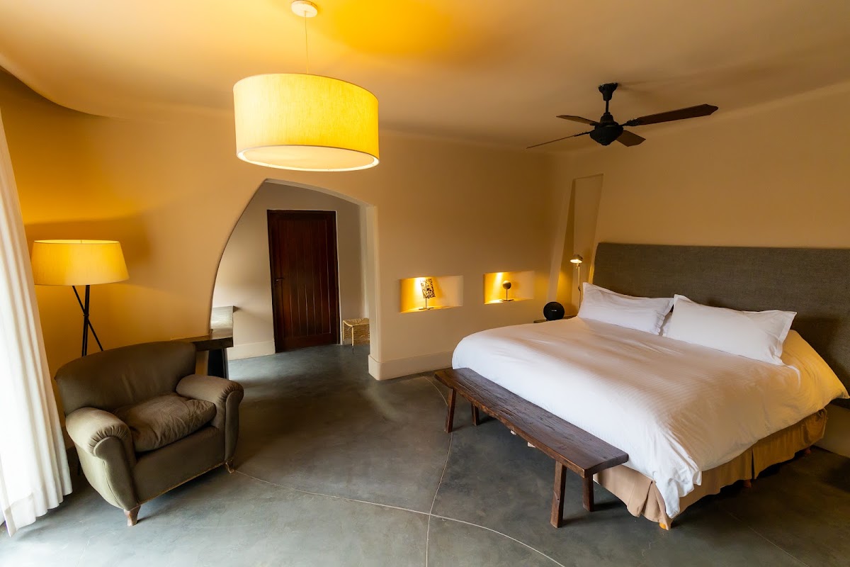Resort suite with queen bed, leather armchair, pendant light fixture, and warm ambient lighting throughout the room.