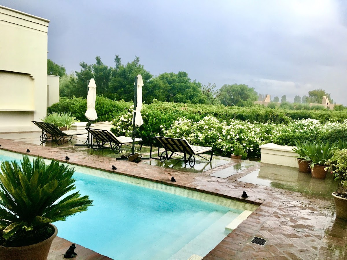 Pool deck at Awasi Mendoza with loungers, white umbrellas, and flowering gardens beyond.