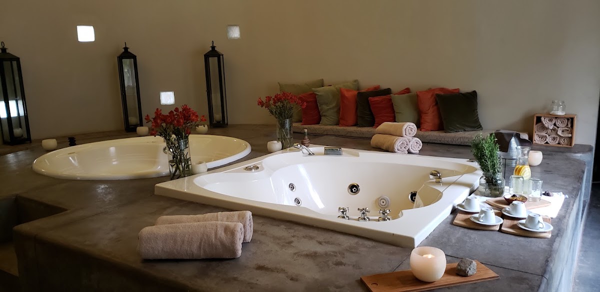 Spa bathroom with two soaking tubs, rolled towels, red flowers, and a seating area with colorful pillows at Awasi Mendoza.