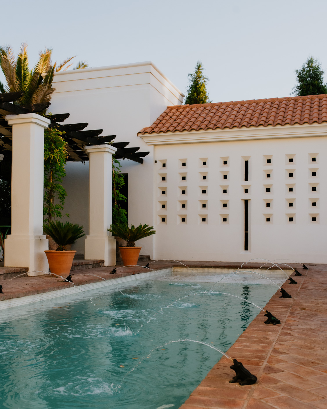 Rectangular pool with turquoise water beside white colonial-style building with terracotta roof and columned pergola at Awasi Mendoza.