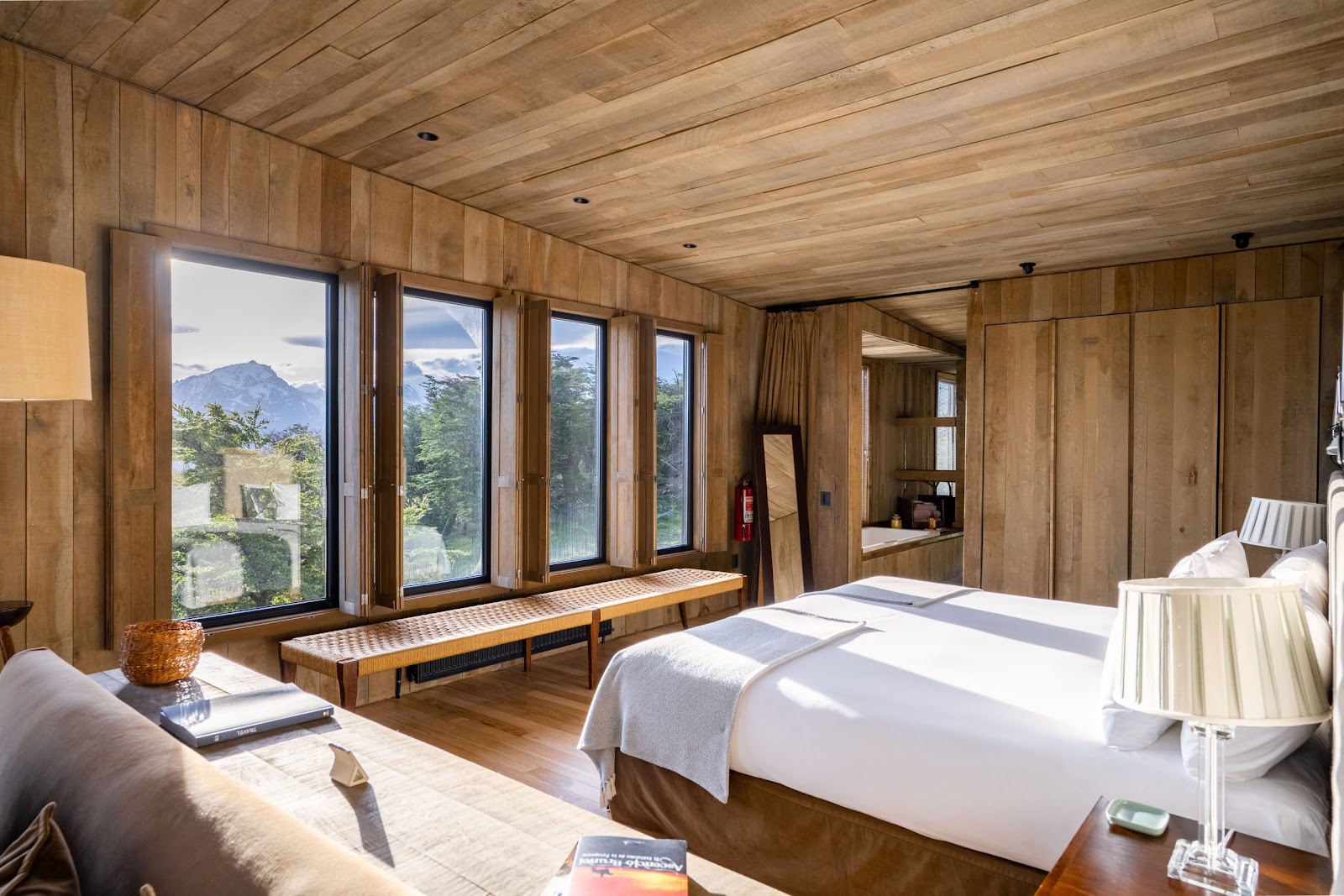 Wood-paneled bedroom with two beds, large windows overlooking mountains and forest at Awasi Patagonia.