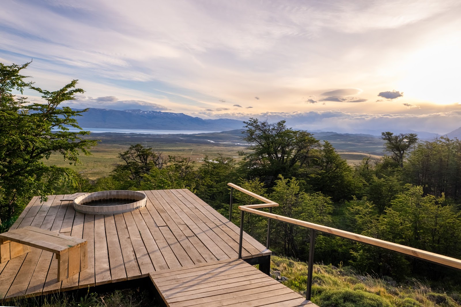 Guest soaks in an outdoor wooden tub on a deck overlooking a sprawling valley and windswept trees at Awasi Patagonia.