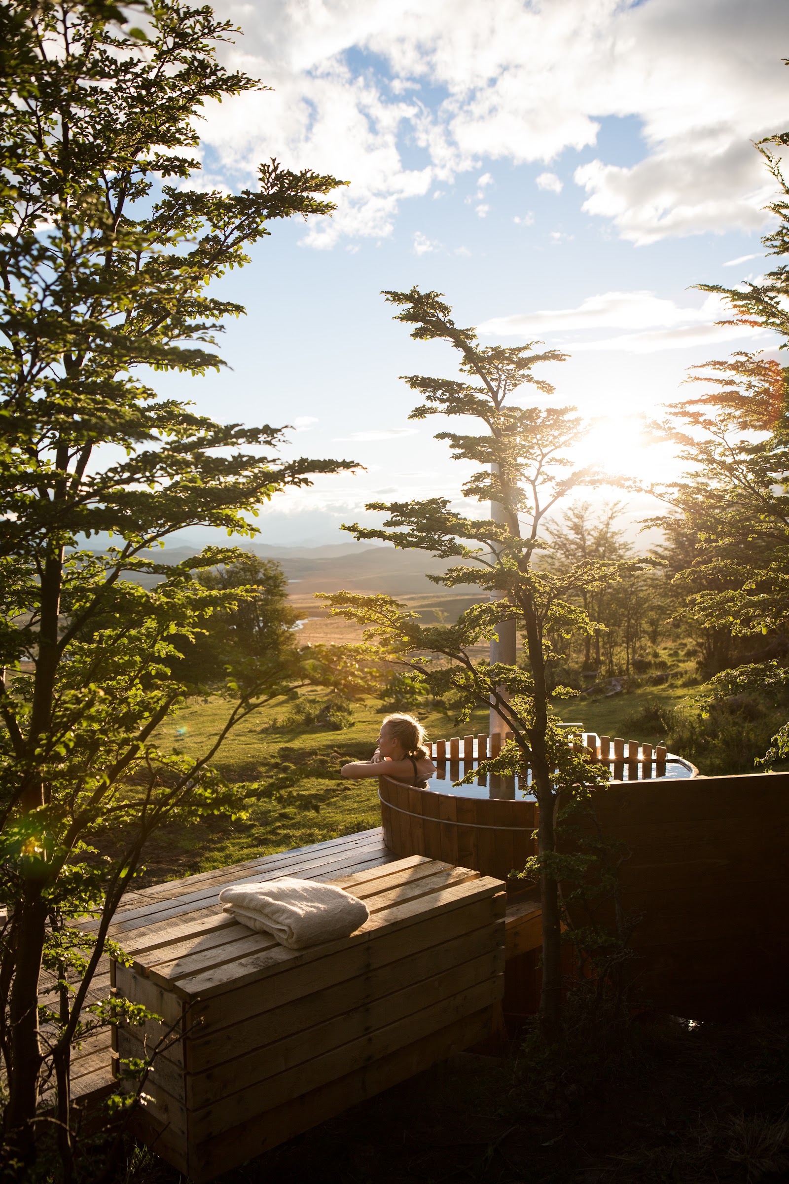 Wooden hot tub nestled among golden autumn trees with towels and firewood nearby, mountain peaks visible in the distance at Awasi Patagonia.