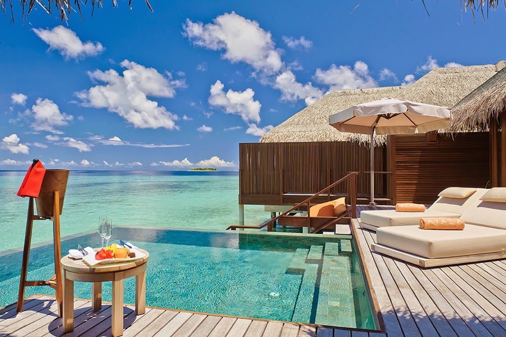 Overwater bungalow at Ayada Maldives with loungers, umbrella, and turquoise lagoon beneath clear blue sky.