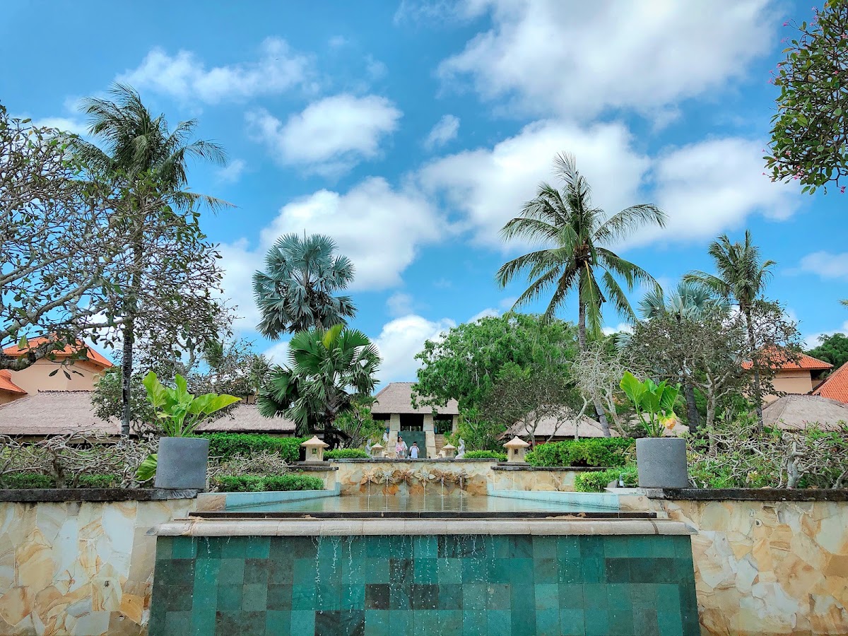 Stone water feature with turquoise pool and cascading water, surrounded by palm trees and tropical landscaping at AYANA Resort Bali.