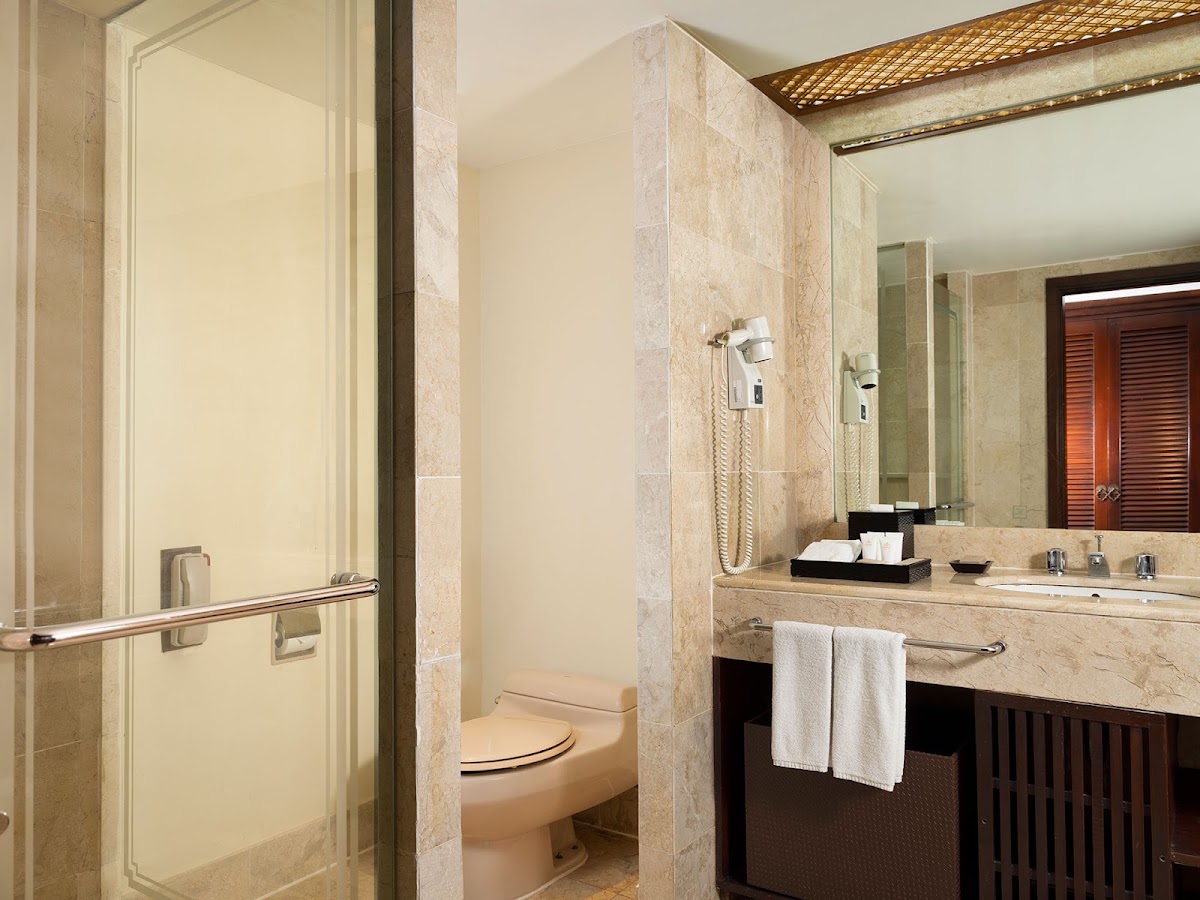 Bathroom with travertine tile walls, double vanity with mirrors, glass shower enclosure, and wooden cabinet details.