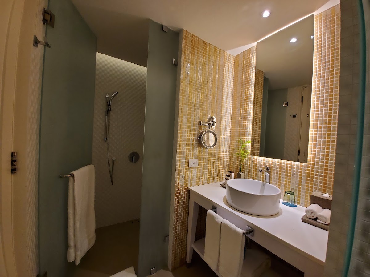 Modern bathroom with golden mosaic tile walls, oval white sink, glass shower enclosure, and illuminated mirror at Azul Beach Resort Negril.