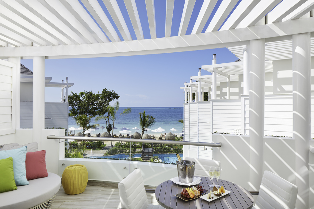 Azul Beach Resort Negril balcony with striped pergola, colorful cushions, and ocean view beyond white cabanas and beach.